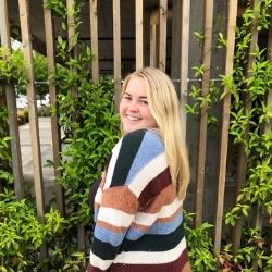 Kate Gularte wearing a striped sweater standing outside by ivy smiling for the camera