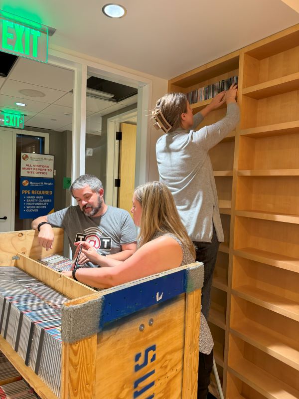 Three people organizing cds and putting them onto built-in wall shelves