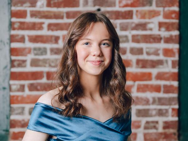 Woman standing in front of a brick wall - 2024 Young Artist in Residence Elaina Stuppler