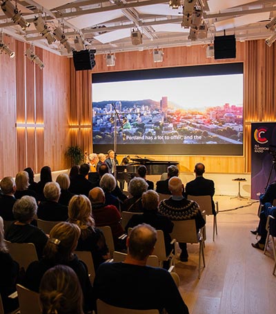 Performance hall full of people watching a video on a large screen