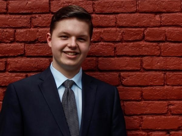 Cameron Massey standing against a red brick wall in a suit